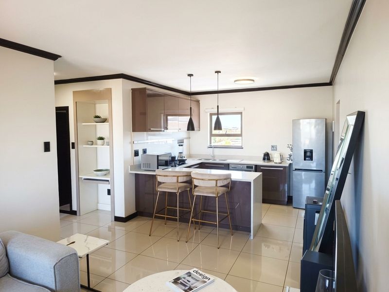 Modern open-plan kitchen featuring sleek glossy cabinetry, stone countertops, and tiled flooring, seamlessly integrated with the living area.