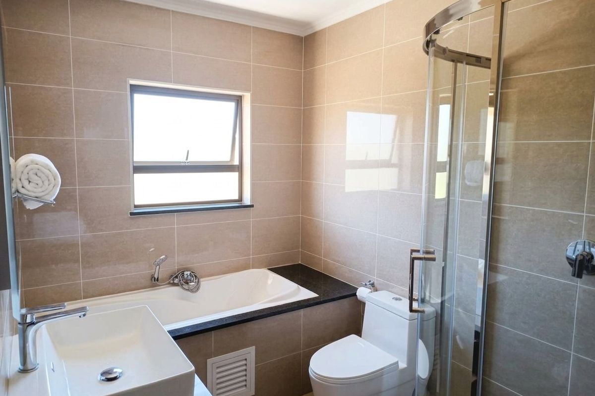 Modern bathroom featuring a built-in bathtub, separate glass shower enclosure, wall-mounted basin, and neutral floor-to-ceiling tiling.