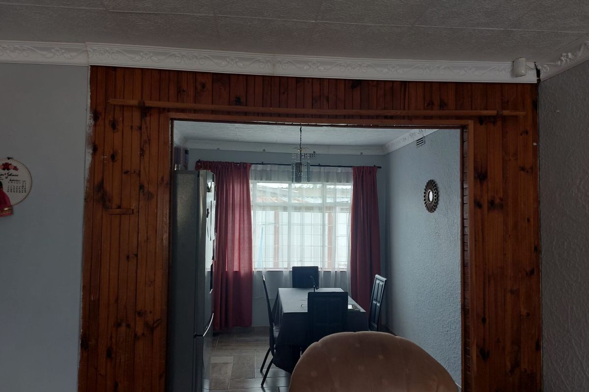 A view through a wood-paneled doorway into a dining area featuring tiled flooring and natural light from a window.