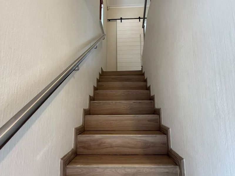 A clean, modern staircase featuring wood-look laminate treads, a sleek metal handrail, and a contemporary sliding barn door at the landing.