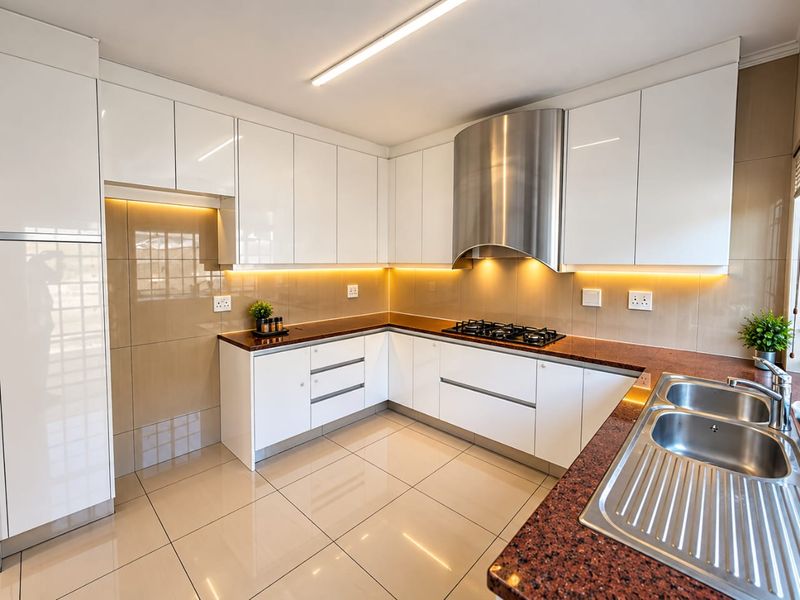 Modern kitchen featuring high-gloss white cabinetry, granite countertops, integrated gas hob, stainless steel extractor fan, and sleek tiled finishes throughout.