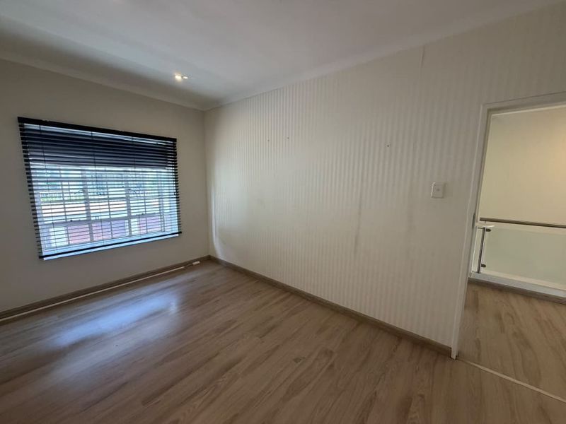 An empty bedroom featuring laminate flooring, venetian blinds, and neutral wall finishes, offering a blank canvas for personalization.