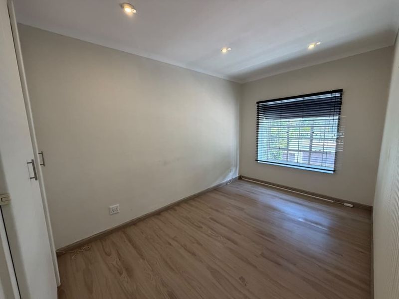 An empty bedroom featuring light laminate flooring, built-in cupboards, recessed downlighting, and venetian blinds on the window.