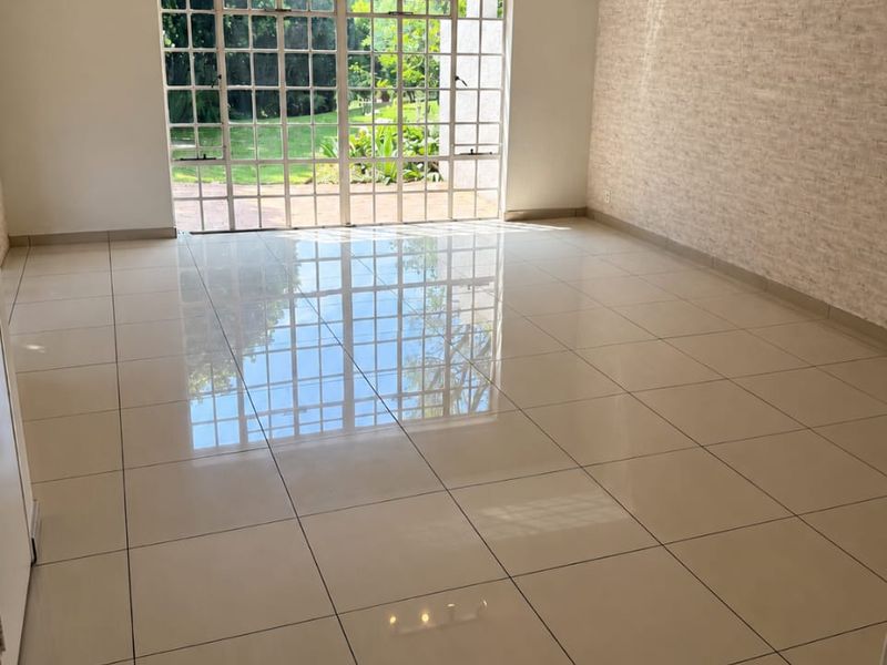 Spacious, light-filled living area featuring polished tiled floors, a textured feature wall, and large glass doors providing direct access to the garden.
