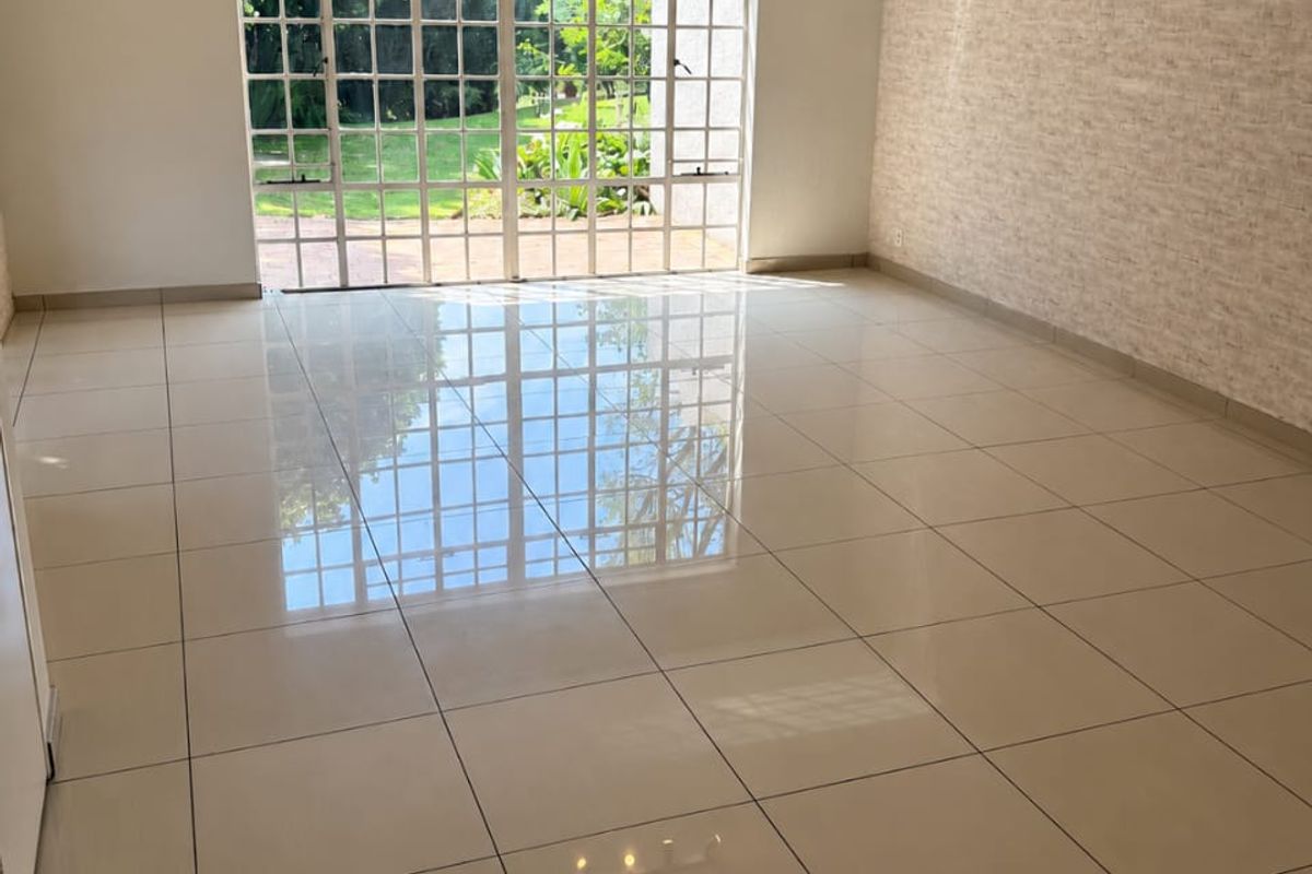 Spacious, light-filled living area featuring polished tiled floors, a textured feature wall, and large glass doors providing direct access to the garden.
