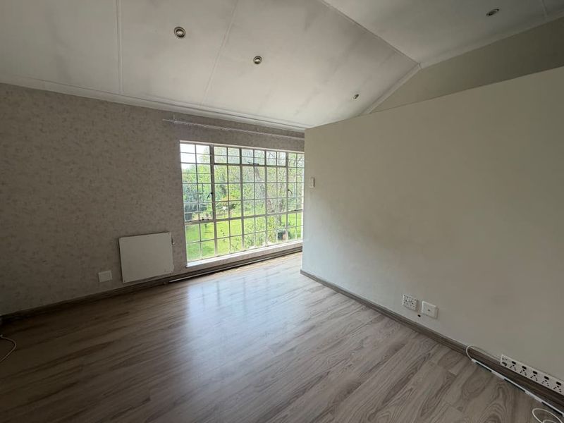 An empty bedroom featuring laminate flooring, a large steel-framed window, a wall-mounted radiator, and a vaulted ceiling with recessed lighting.