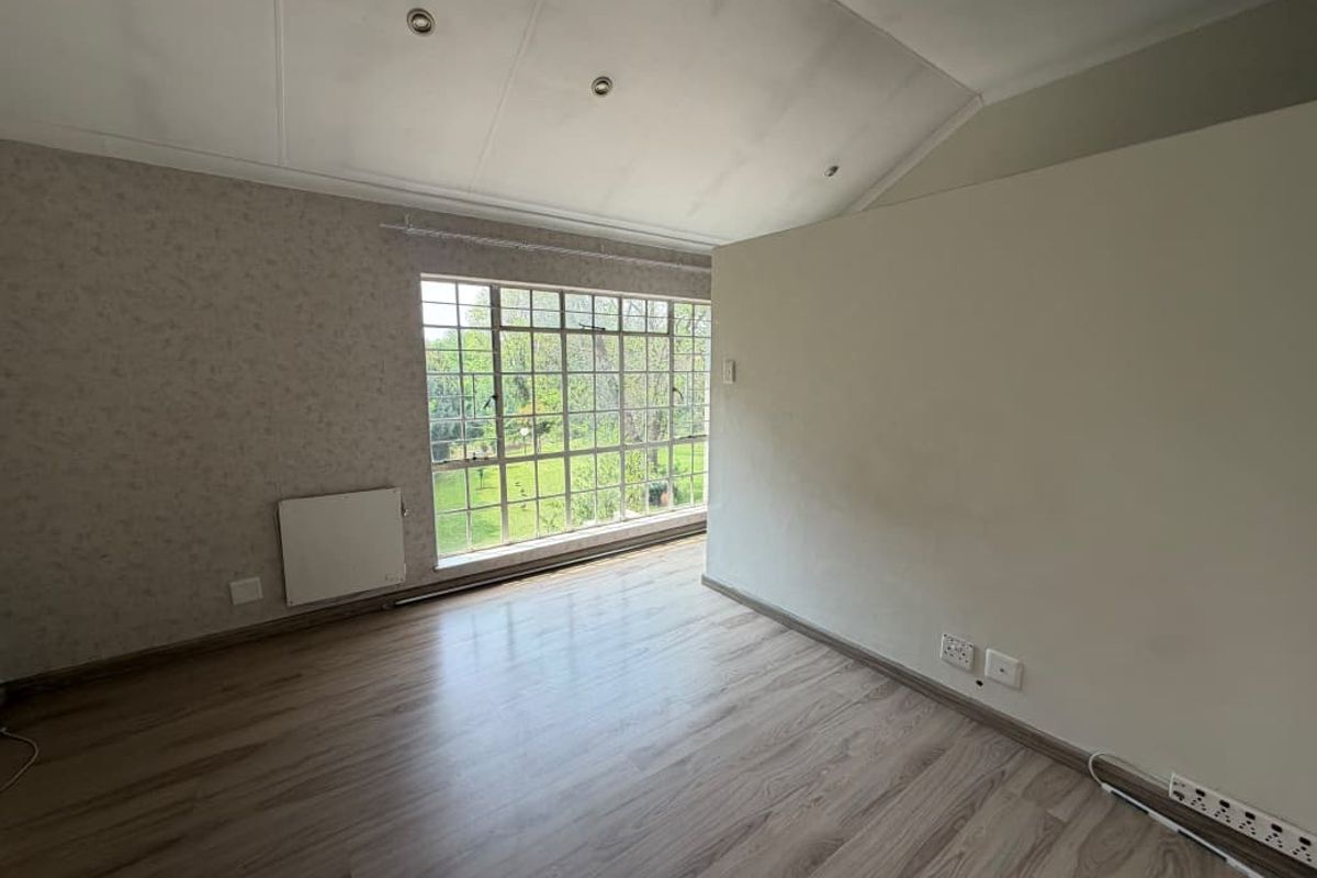 An empty bedroom featuring laminate flooring, a large steel-framed window, a wall-mounted radiator, and a vaulted ceiling with recessed lighting.