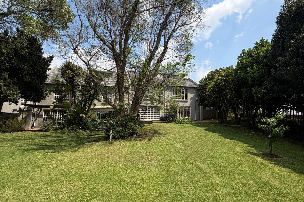 A spacious rear garden featuring a well-maintained lawn, mature trees, and a view of the rear building facade with multi-pane windows.