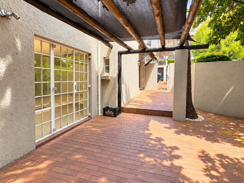 A private outdoor patio area featuring brick paving, a timber pergola with shade cloth, and direct access to the interior through french doors.