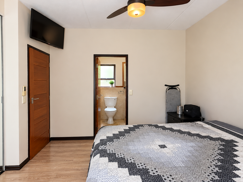 A well-maintained bedroom featuring laminate flooring, a ceiling fan, and mirrored sliding wardrobe doors, with direct access to an en-suite bathroom.