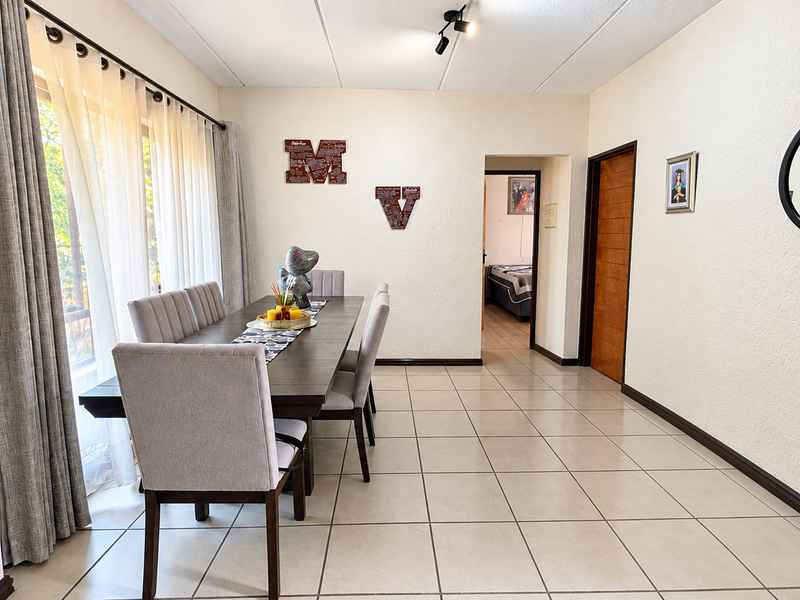 A dining room featuring tiled flooring, a sliding glass door with curtains, and an intercom system, providing access to an adjacent bedroom.