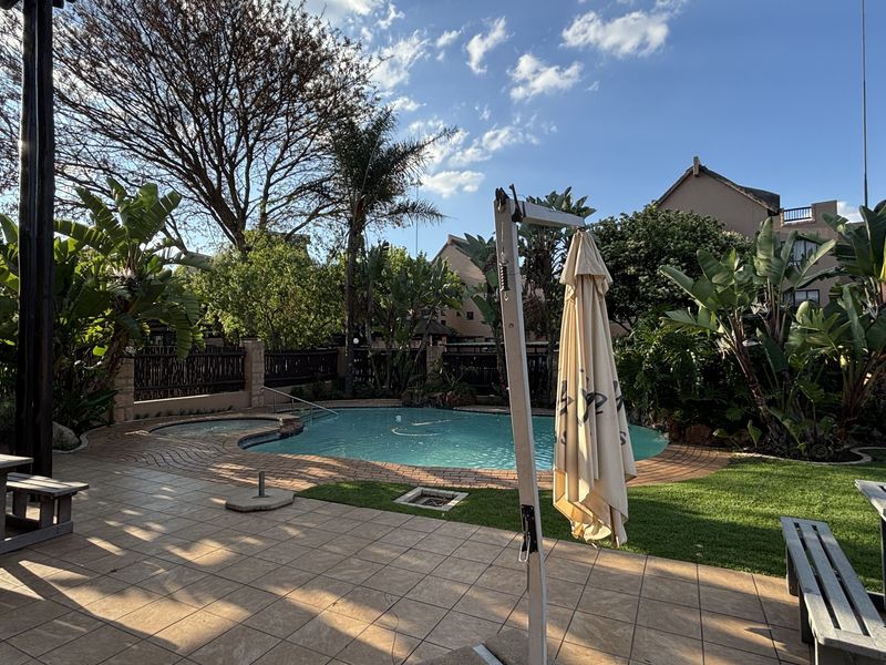 A well-maintained outdoor pool area featuring a tiled patio, landscaped garden, and a built-in spa, perfect for relaxation and outdoor entertainment.