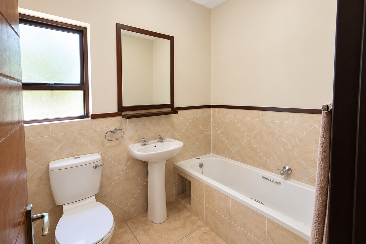 A clean and functional bathroom featuring a pedestal basin, bathtub, toilet, and neutral wall tiling with a wooden-framed mirror.