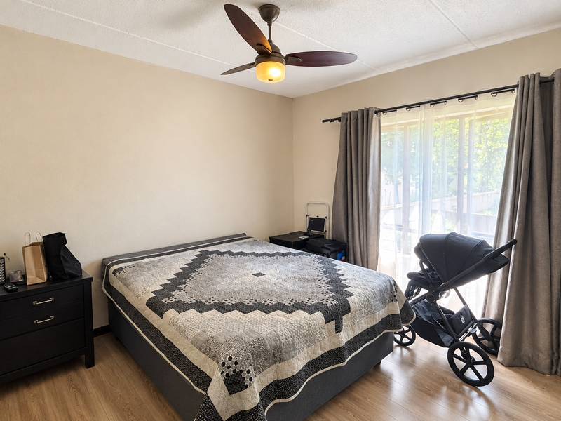A bedroom featuring laminate flooring, a ceiling fan, and a sliding glass door providing natural light.