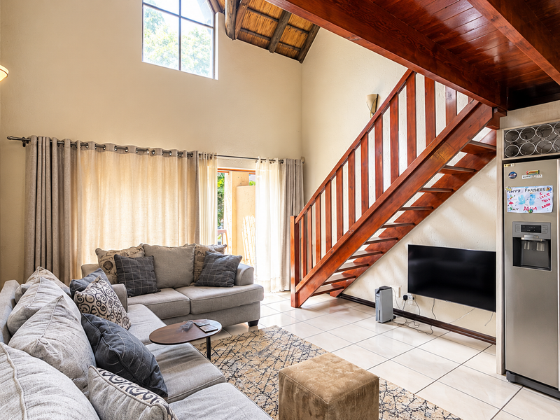 Spacious living area featuring a double-volume vaulted ceiling with exposed timber beams, a wooden staircase, and large windows providing ample natural light.