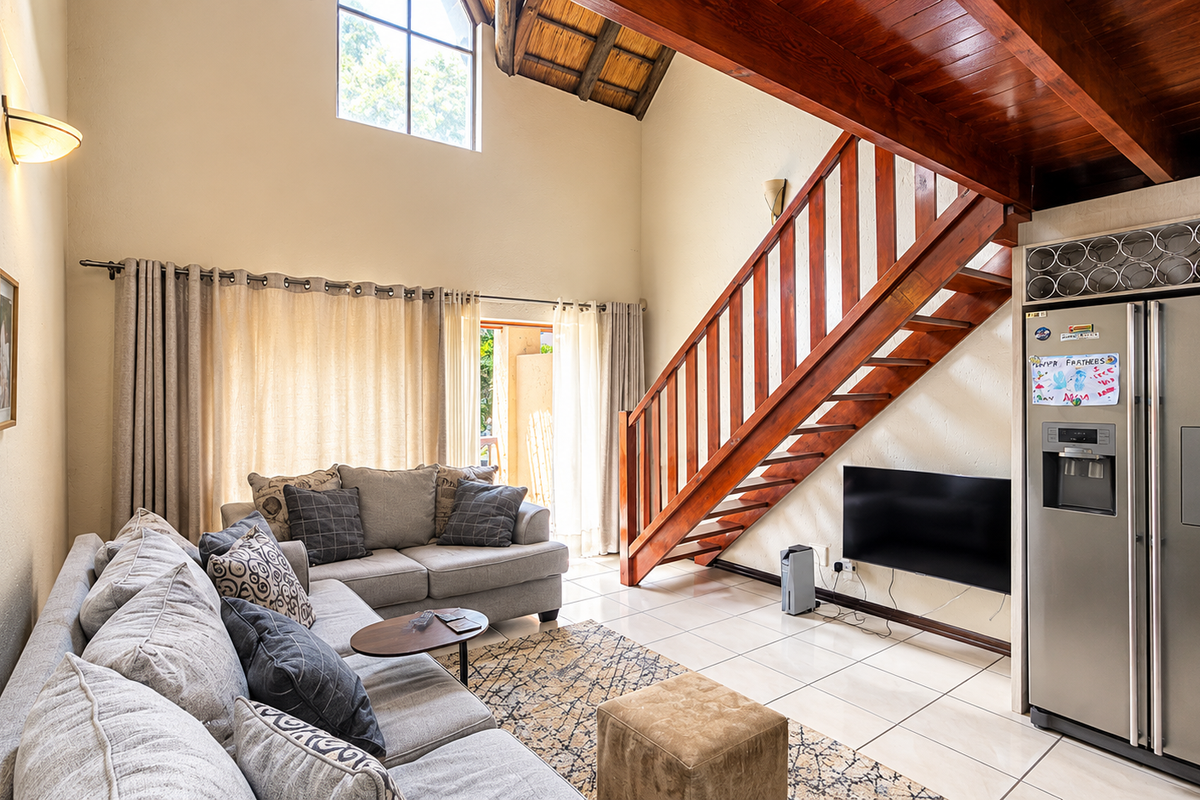 Spacious living area featuring a double-volume vaulted ceiling with exposed timber beams, a wooden staircase, and large windows providing ample natural light.