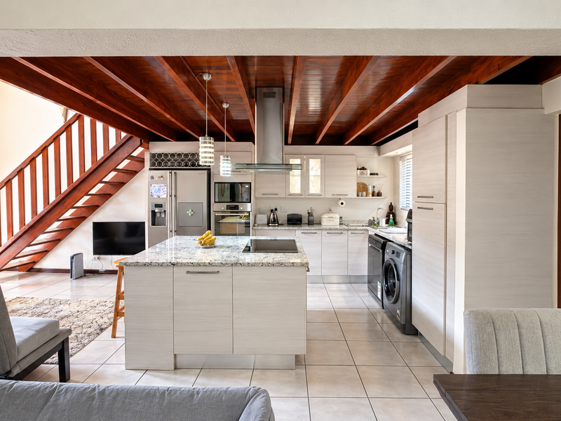 Spacious open-plan kitchen and living area featuring a central island, granite countertops, modern built-in appliances, and striking exposed timber ceiling beams.