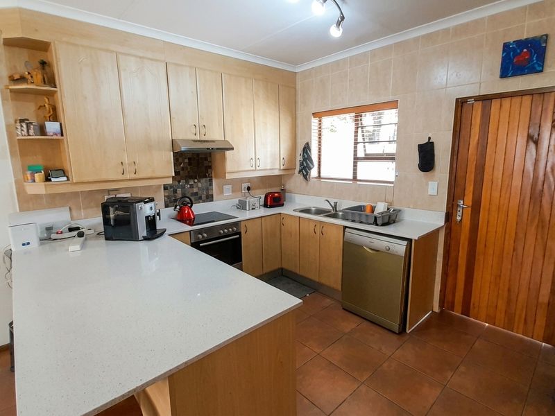 A functional kitchen featuring light wood cabinetry, stone countertops, tiled flooring, and integrated appliances, offering a practical layout for daily meal preparation.