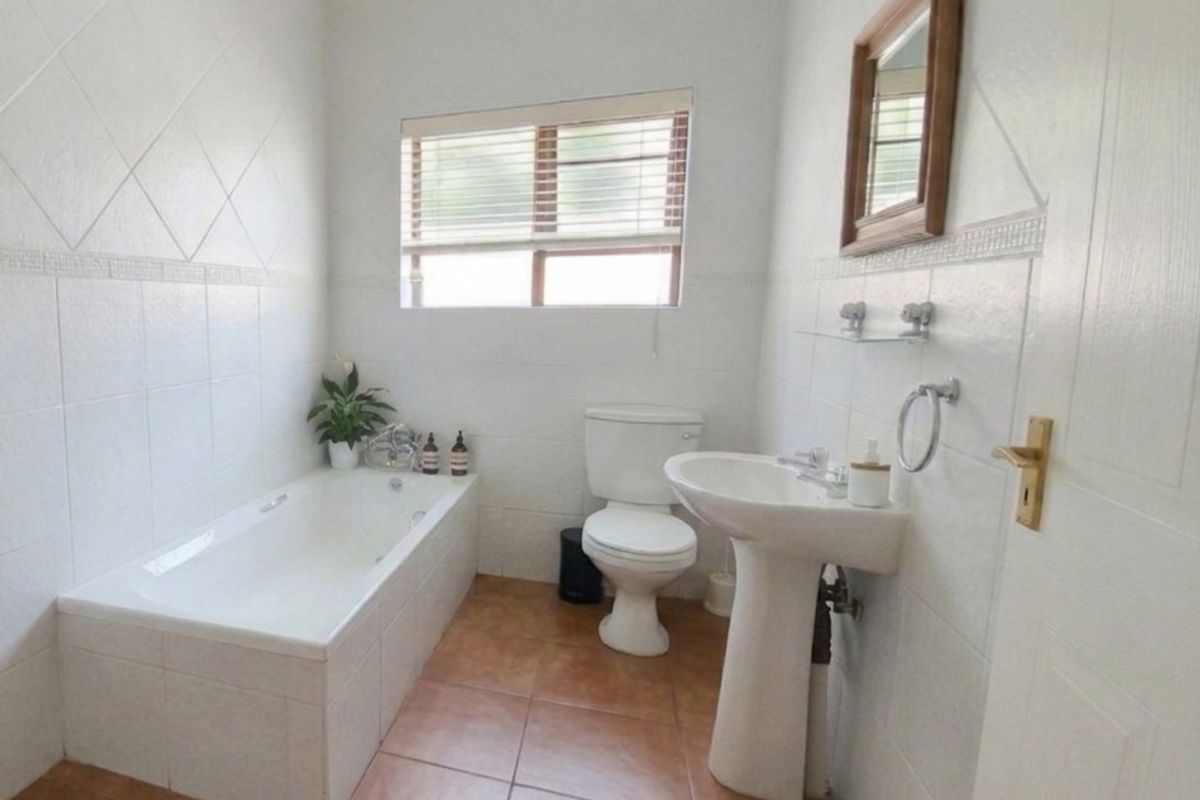 A functional bathroom featuring a built-in bathtub, pedestal washbasin, and toilet, finished with tiled walls and flooring.