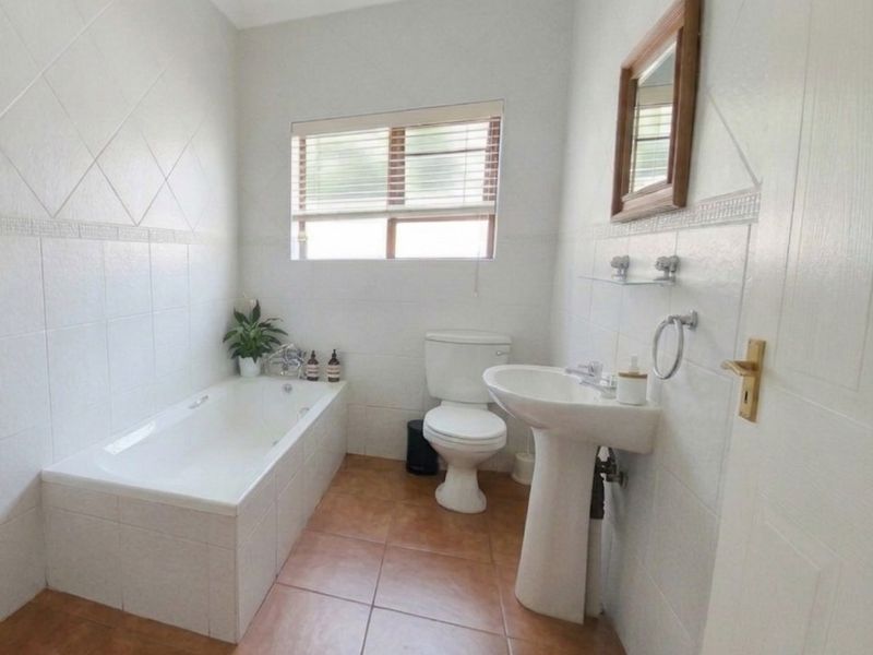 A functional bathroom featuring a built-in bathtub, pedestal washbasin, and toilet, finished with tiled walls and flooring.