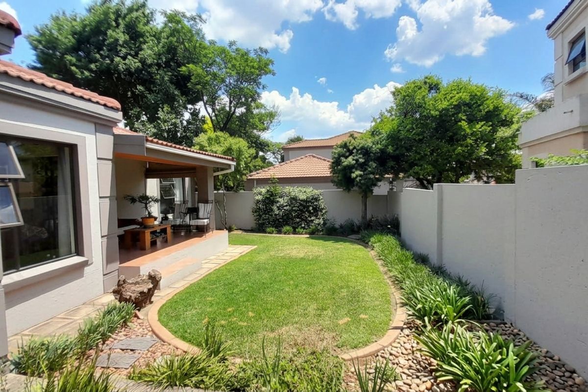 A well-maintained rear garden featuring a manicured lawn, landscaped borders, and a covered patio area, enclosed by solid perimeter walls.