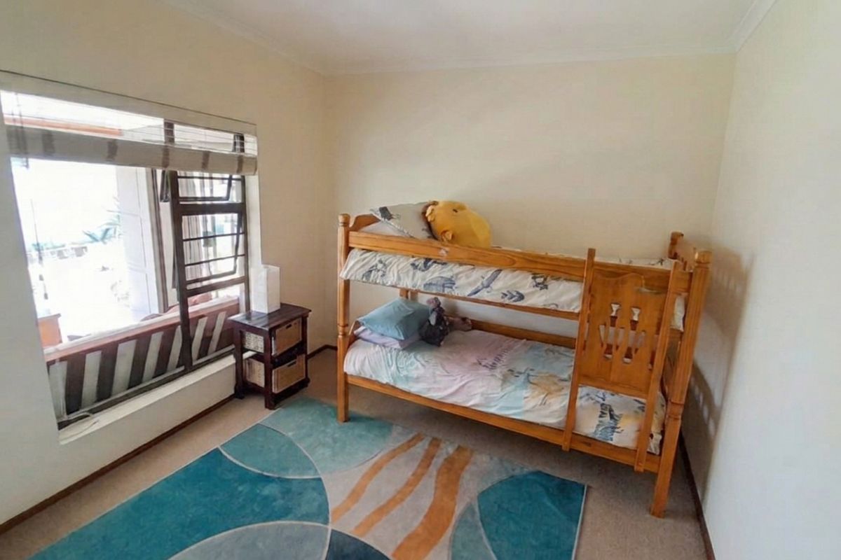 A functional bedroom featuring carpeted flooring and a large window with integrated security bars, providing natural light and ventilation.