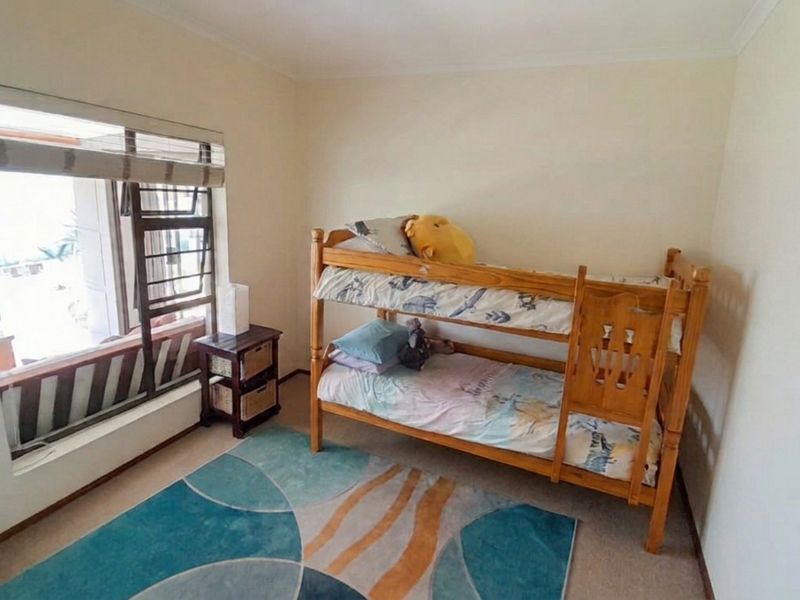 A functional bedroom featuring carpeted flooring and a large window with integrated security bars, providing natural light and ventilation.