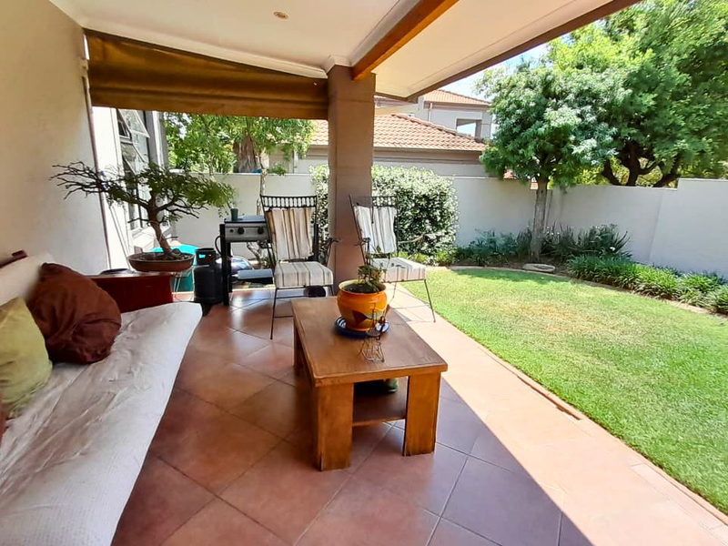 A covered patio area featuring tiled flooring and recessed lighting, overlooking a private garden with a well-maintained lawn and boundary wall.