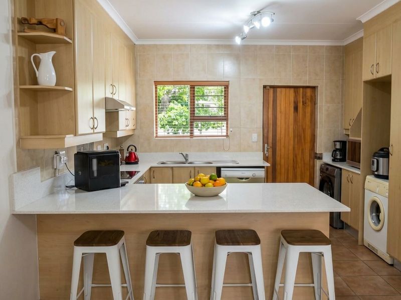 A functional kitchen featuring light wood cabinetry, stone countertops, a breakfast bar, and tiled finishes, offering a practical layout with integrated appliance space.