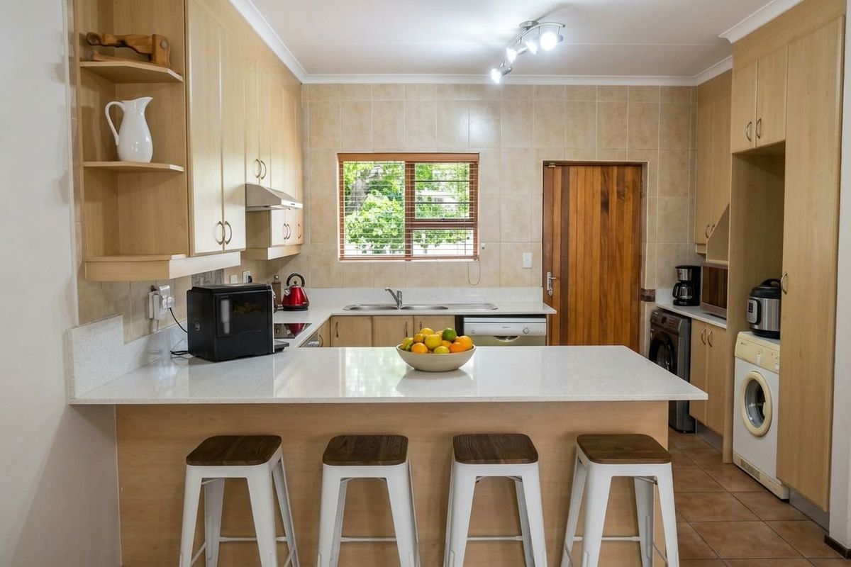 A functional kitchen featuring light wood cabinetry, stone countertops, a breakfast bar, and tiled finishes, offering a practical layout with integrated appliance space.
