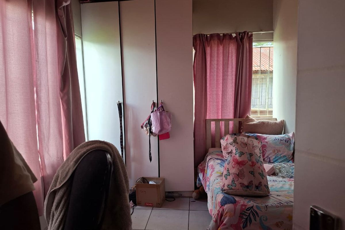 A functional bedroom featuring built-in floor-to-ceiling wardrobes, tiled flooring, and natural light from dual windows.