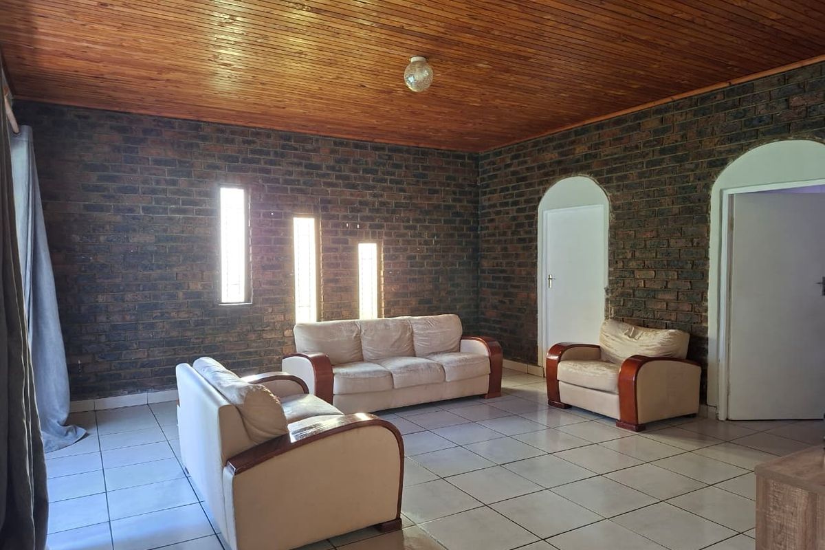 Spacious living room featuring exposed face-brick walls, a timber-paneled ceiling, and tiled flooring with arched doorways leading to adjacent rooms.
