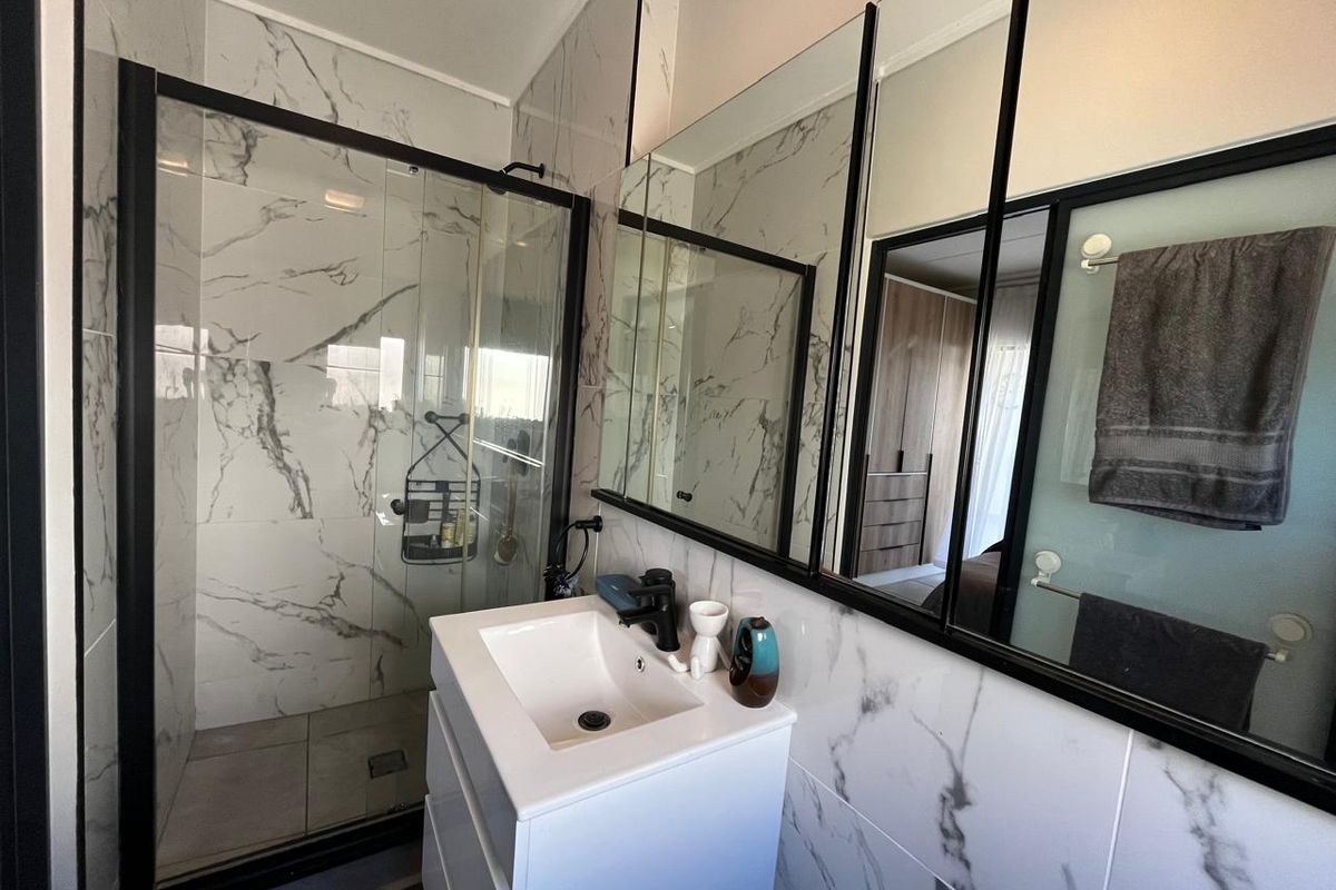 Modern bathroom featuring a walk-in shower with black-framed glass enclosure, marble-look wall tiles, and a sleek vanity with black tapware.
