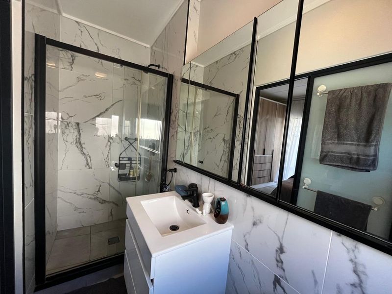 Modern bathroom featuring a walk-in shower with black-framed glass enclosure, marble-look wall tiles, and a sleek vanity with black tapware.