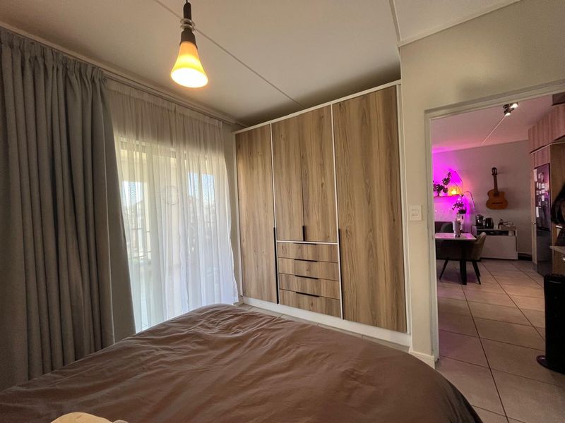 A well-maintained bedroom featuring modern wood-finish built-in wardrobes, tiled flooring, and direct access to an adjoining living area.