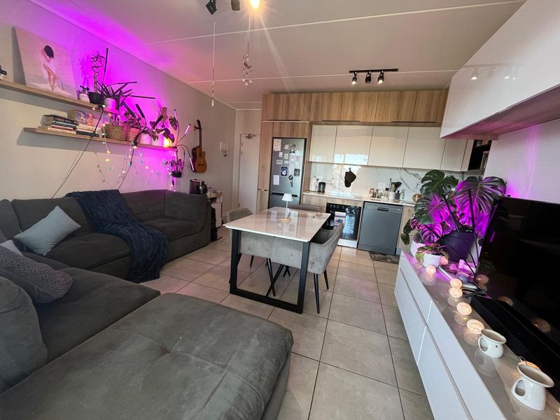 Modern open-plan living and kitchen area featuring contemporary cabinetry, integrated appliances, tiled flooring, and stylish track lighting in a well-maintained apartment setting.