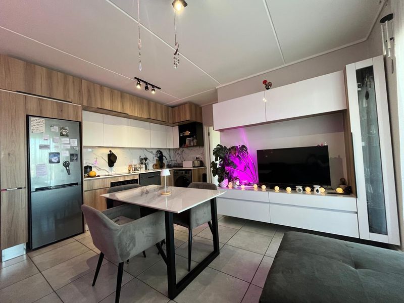 Modern open-plan living area featuring a contemporary kitchen with wood-tone and white cabinetry, marble-look backsplash, and a seamless integrated media wall unit.