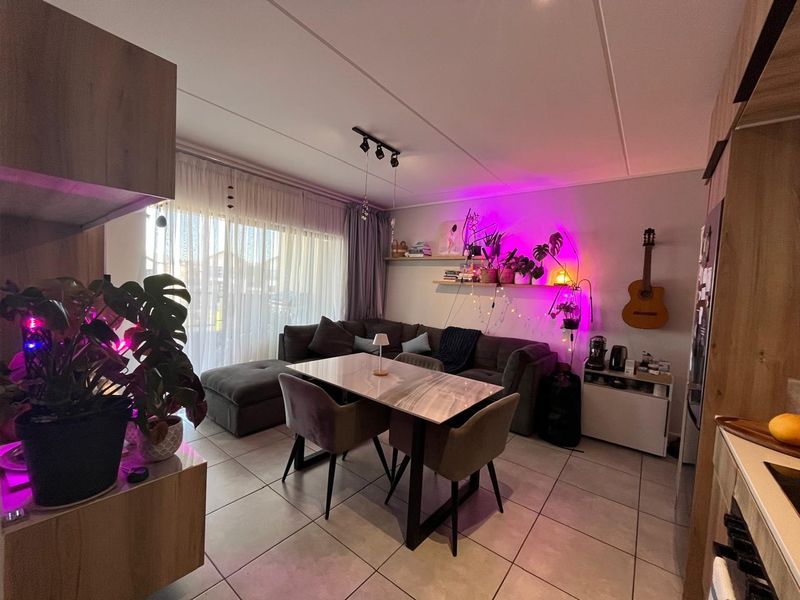 An open-plan living and dining area featuring tiled flooring, modern track lighting, and large sliding glass doors that provide ample natural light.