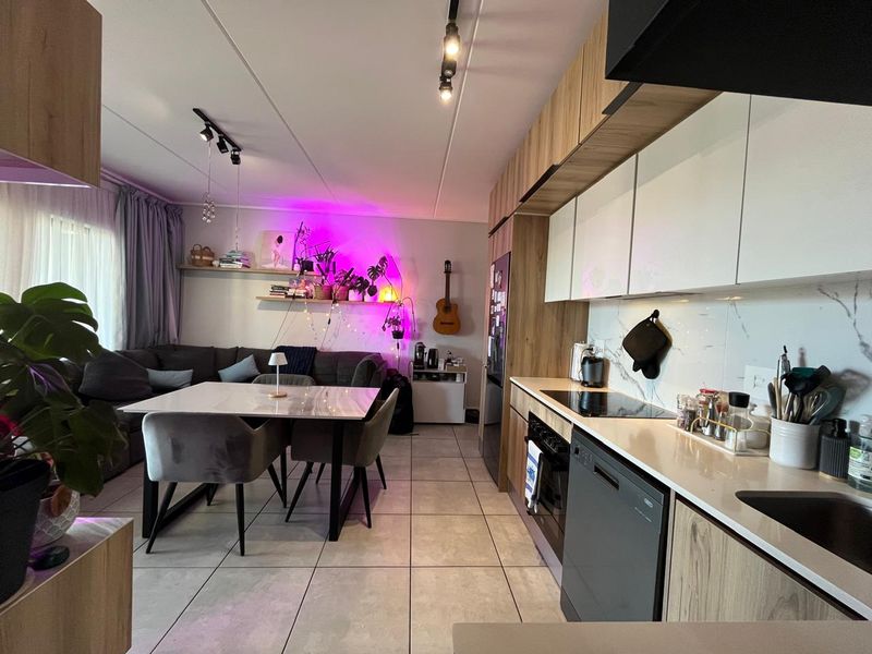 Modern open-plan living and kitchen area featuring contemporary cabinetry, stone countertops, integrated appliances, and sleek tiled flooring throughout.