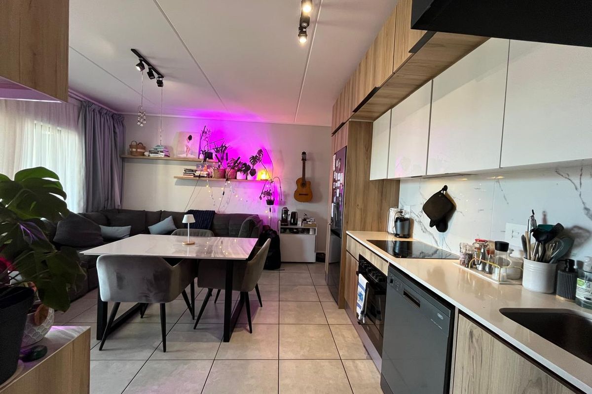 Modern open-plan living and kitchen area featuring contemporary cabinetry, stone countertops, integrated appliances, and sleek tiled flooring throughout.