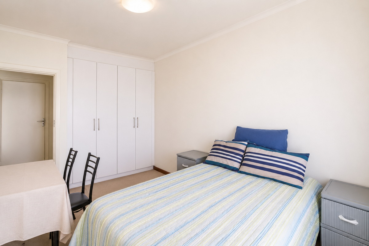 A functional bedroom featuring neutral walls, carpeted flooring, and a large white built-in wardrobe providing ample storage space.
