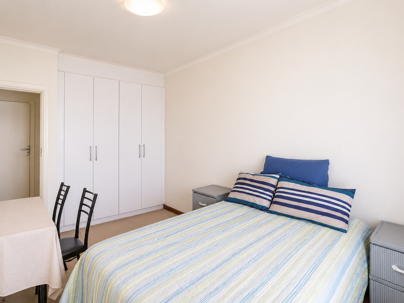 A functional bedroom featuring neutral walls, carpeted flooring, and a large white built-in wardrobe providing ample storage space.