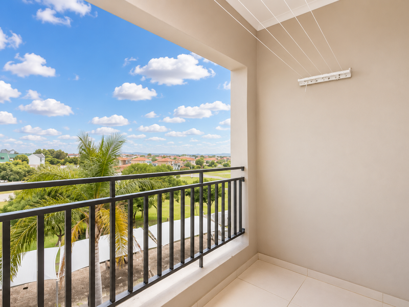 A clean, covered balcony featuring a metal balustrade, tiled flooring, and a retractable clothesline, offering pleasant views of the surrounding neighborhood.