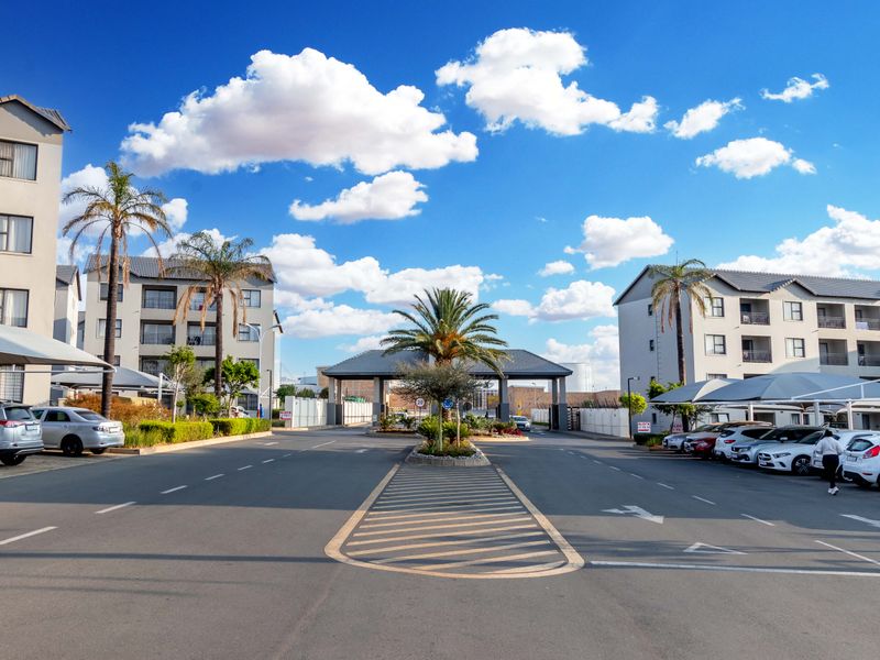 View of the apartment complex entrance featuring a secure gatehouse, paved driveway, and covered parking facilities for residents.