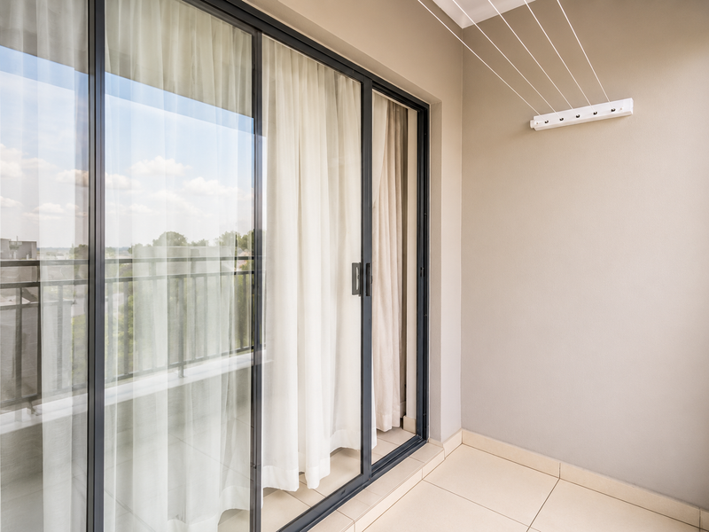 A clean, modern balcony featuring large sliding glass doors, neutral tiled flooring, and a convenient wall-mounted retractable clothesline.