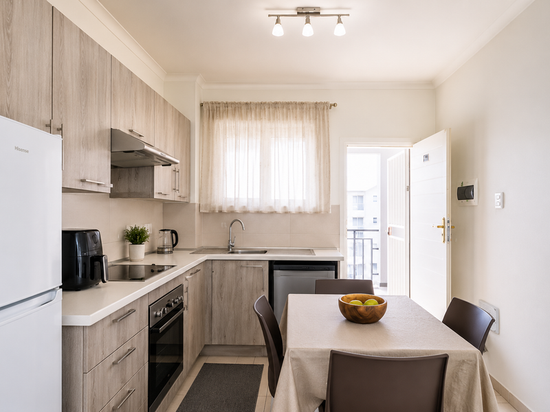 A well-maintained open-plan kitchen featuring light wood-grain cabinetry, modern built-in appliances, and a functional dining area with direct access to a balcony.