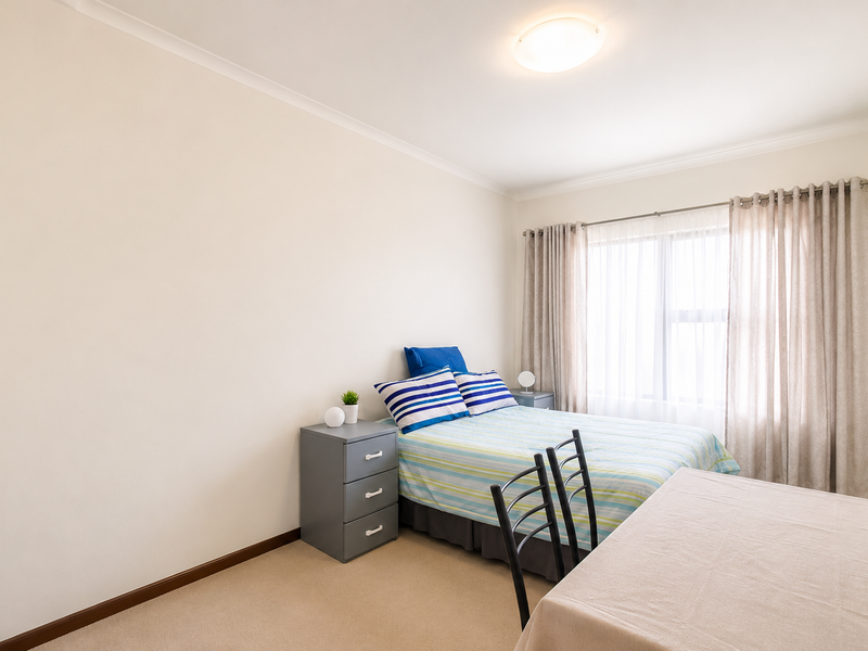 A well-lit bedroom featuring neutral wall tones, carpeted flooring, and large windows with installed curtain tracks.