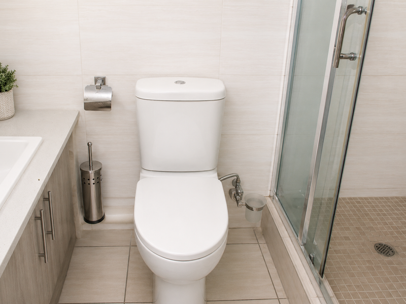 A modern bathroom featuring a vanity with stone countertop, a white toilet, and a glass-enclosed shower with neutral wall and floor tiling.