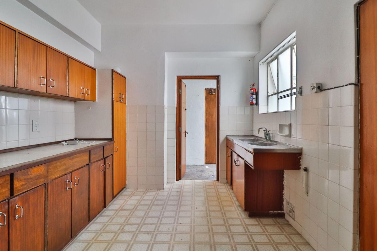A dated kitchen featuring original wooden cabinetry, tiled splashbacks, and a stainless steel sink, offering a blank canvas for modern renovation.