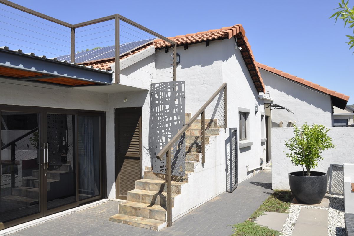 Rear exterior view featuring a paved patio, external staircase with metal railing, solar panels on the roof, and sliding glass door access.